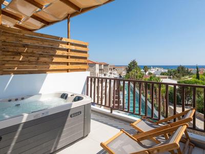 Terrasse mit Whirlpool, zwei Liegestühlen, Holzgeländer und Blick auf Stadt und Meer.