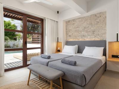 Schlafzimmer mit grauem Bett, zwei Handtüchern, Holzbank, Beistelltischen und großen Glastüren.
