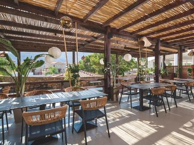 Offener Restaurantbereich mit Holzdach, Tischen und Stühlen, Pflanzen und natürlichem Licht.