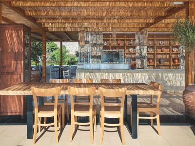 Rustikale Außenterrasse mit Holztisch, sechs Holzstühlen und Bar mit Bambusdach und Pflanzen.