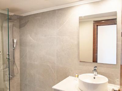 Helle, moderne Dusche mit Glasabtrennung, rundem Waschbecken, Spiegel und Handtüchern auf Holzablage.
