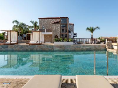 Modernes Haus mit großem Pool, Palmen und Terrasse, klarer blauer Himmel, ruhige Atmosphäre.