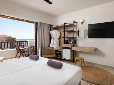 Modernes Hotelzimmer mit Doppelbett, Fernseher, offener Terrasse und Meerblick bei Tageslicht.