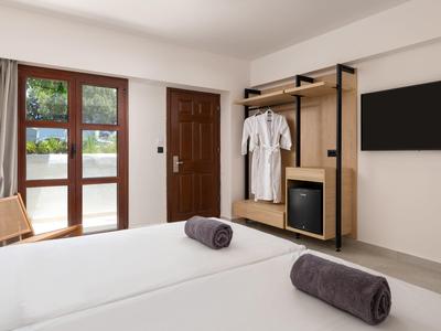 Hell eingerichtetes Hotelzimmer mit großen Fenstern, Tür, Kleiderständer und Flachbildfernseher.