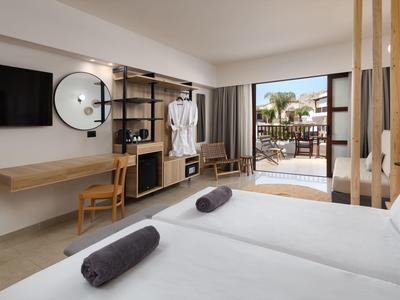 Modernes Hotelzimmer mit Doppelbett, Holzmöbeln und Terrasse mit Strandblick.