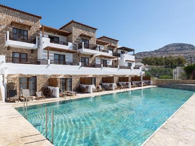 Hotel moderno con piscina, tumbonas y montaña de fondo bajo cielo despejado.