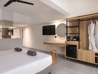 Modernes Hotelzimmer mit Doppelbett, Wand-TV, Holzregal und zwei weißen Bademänteln.