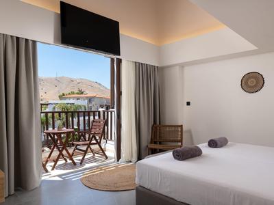 Helles Schlafzimmer mit Doppelbett, zwei Handtüchern, Balkon mit Tisch, Stühlen und Blick auf Berge.