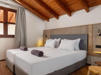 Modernes Schlafzimmer mit großem Bett, Holzbalkendecke und Fenster mit grauem Vorhang.