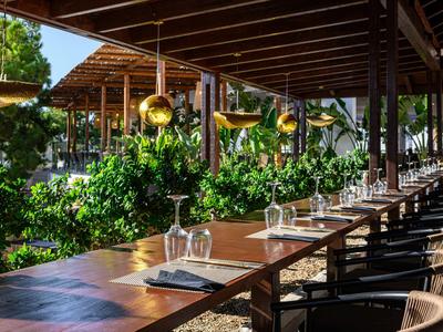 Larga fila de mesas con copas bajo pérgola de madera al aire libre.