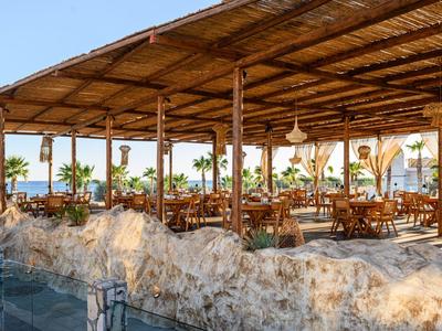 Espace extérieur couvert avec tables et chaises en bois dans un restaurant d'hôtel en bord de mer.