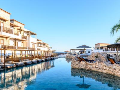Complejo hotelero moderno con piscina y tumbonas bajo un cielo azul.