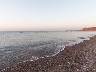 Ruhevolle Küstenlandschaft mit sanften Wellen, Kieselstrand und flachem Ufer vor hellem Himmel.