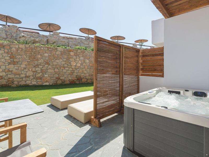 Vasca idromassaggio moderna all'aperto con ombrelloni e lettini sullo sfondo.