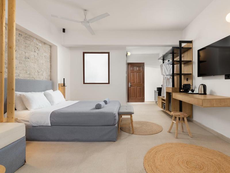 Camera d'hotel moderna con letto matrimoniale, scrivania, TV e arredamento minimalista.