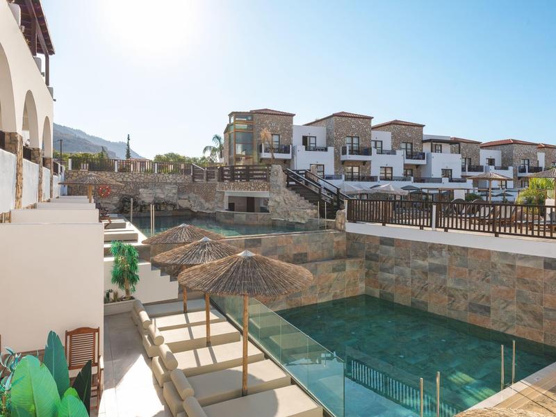 Complesso alberghiero moderno con piscina, ombrelloni e edifici terrazzati sotto un cielo limpido.