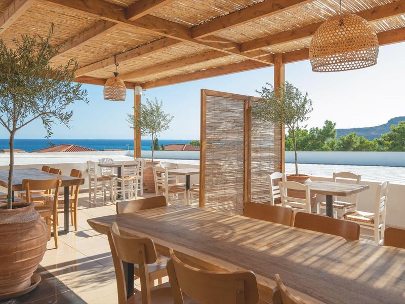 Terrazza coperta con mobili in legno e vista sul mare sotto un cielo limpido.