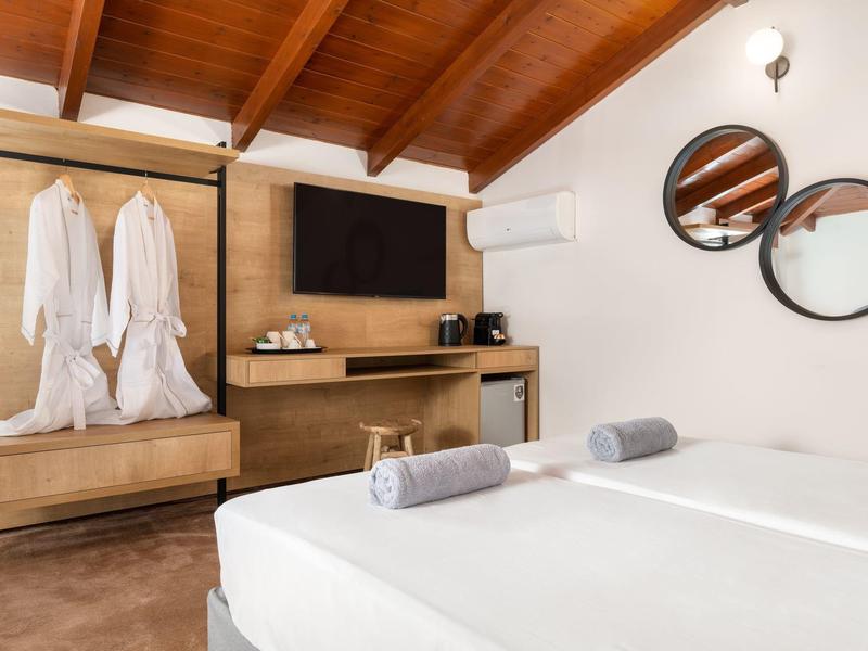 Camera d'hotel moderna con soffitto a travi in legno, letto matrimoniale e armadio aperto con accappatoi.