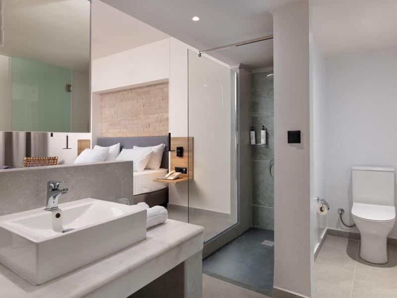 Camera d'hotel moderna con lavandino, doccia e toilette in colori chiari e luminosi.