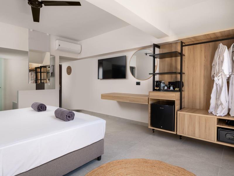 Camera d'albergo moderna con letto bianco, TV a parete, mobili in legno e bagno sullo sfondo.