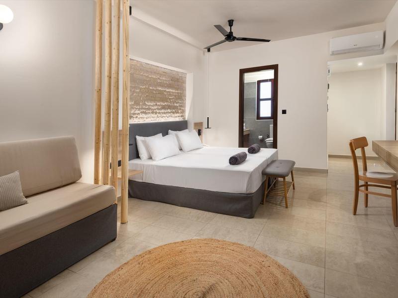 Camera d'hotel moderna con letto matrimoniale, divano, mobili in legno e toni neutri.