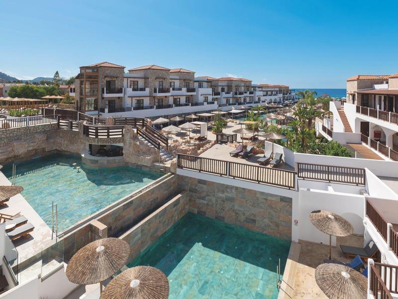 Vista di un hotel di lusso con piscine private e mare sullo sfondo, ombrelloni presenti.
