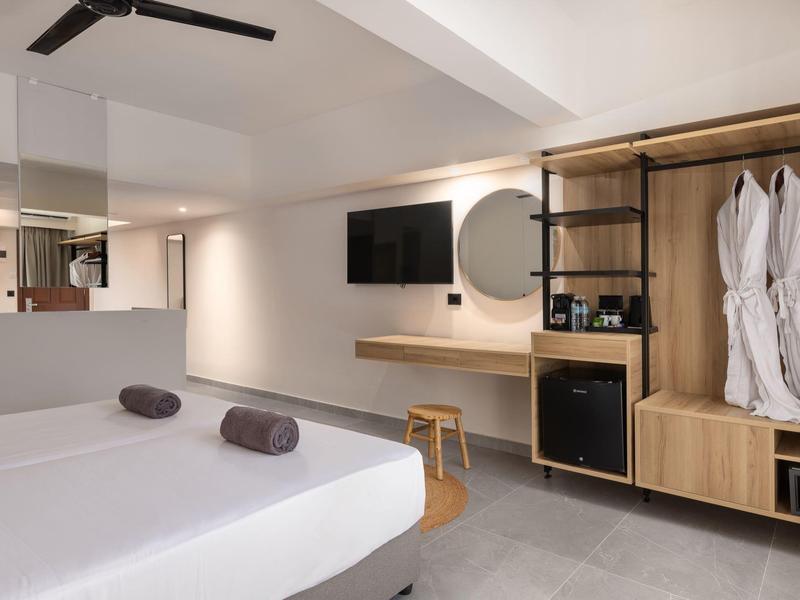 Camera d'hotel moderna con due letti, TV a parete, sgabelli e guardaroba aperto con accappatoi.