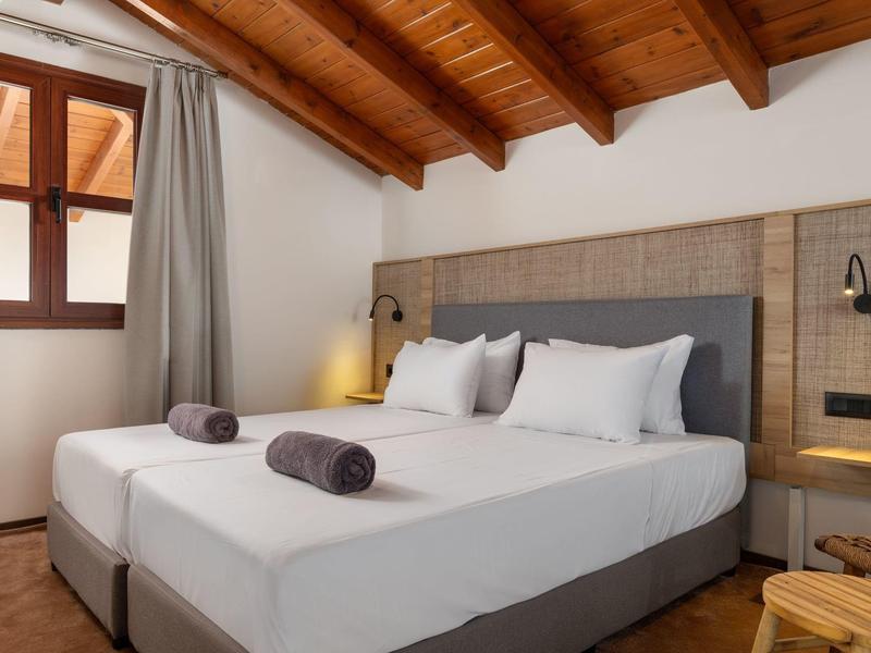 Camera d'hotel moderna con letto matrimoniale, soffitto in legno e decorazioni neutre.