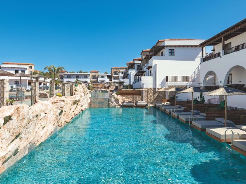Piscina moderna dell'hotel con lettini e edifici bianchi sotto un cielo azzurro.
