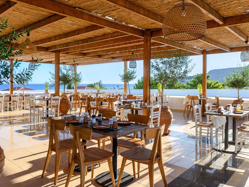 Zona pranzo aperta e soleggiata con mobili in legno in un hotel vicino all'acqua e alle montagne.