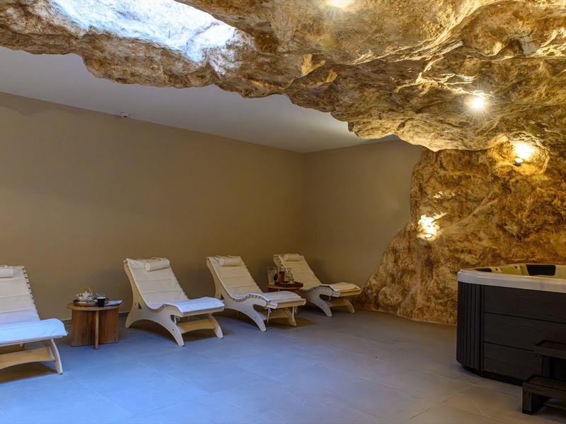 Spa moderno con parete a grotta, sedie a sdraio e vasca idromassaggio in una stanza tranquilla.