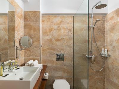 Modernes Badezimmer mit braunen Fliesen, Glasdusche, weißem Waschbecken und Spiegel.