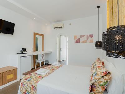 Helles Schlafzimmer mit Doppelbett, floralem Bettbezug, Schreibtisch, Wand-TV und Klimaanlage.