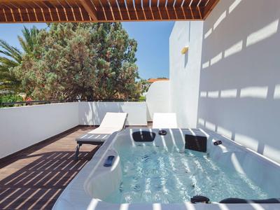 Moderner Außenbereich mit Whirlwanne, Sonnenliegen und Pergola, Sonnenschatten auf weißen Wänden.
