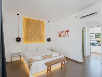 Hell eingerichtetes Schlafzimmer mit Doppelbett, Holzbank, moderner Wandkunst und Blick auf Balkon.