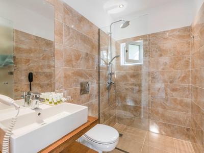 Modernes Badezimmer mit braunen Fliesen, großer Spiegel, Waschtisch, Toilette und begehbarer Dusche.