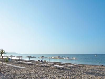 Sandstrand mit Liegestühlen unter weißen Sonnenschirmen, Palmen und blauem Meer im Hintergrund.