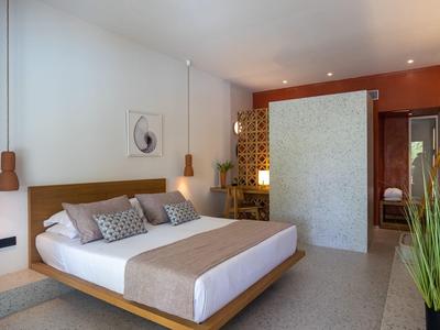 Modernes Schlafzimmer mit großem Bett, Holzmöbeln, Wandlampen und Pflanze im Vordergrund.