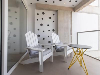 Balkon mit zwei weißen Holzstühlen und kleinem runden Tisch mit gelben Beinen.