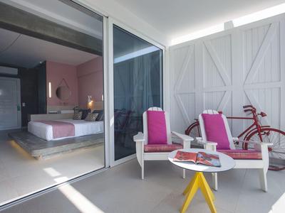 Moderner Balkon mit weißen Stühlen, pinken Kissen, kleinem Tisch und rotem Fahrrad neben Glasschiebetür.