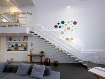 Moderner Wohnraum mit weißer Treppe, grauem Sofa, Holzdekoration und bunter Wandkunst.