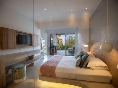 Modernes Schlafzimmer mit Doppelbett, großen Fenstern, Fernseher und direktem Zugang zur Terrasse.