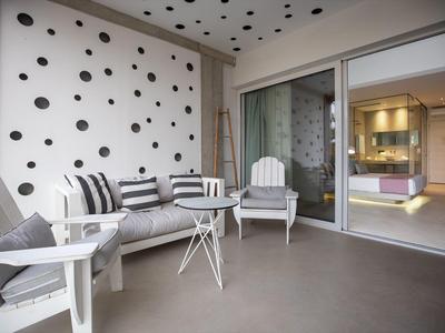 Moderner Balkon mit weißen Holzstühlen, grauer Couch und schwarzem Punktmuster an Wand und Decke.
