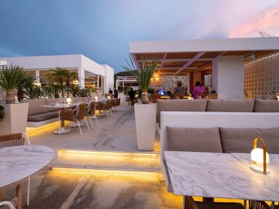 Moderne Terrasse mit weißen Möbeln, Ambientebeleuchtung und Pflanzen bei Abenddämmerung.