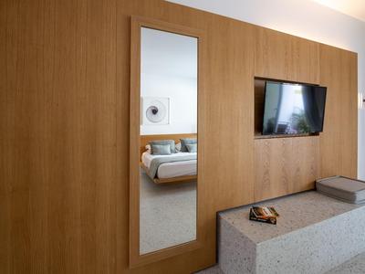 Moderner Hotelzimmerbereich mit Holzpaneelwand, Spiegel, Fernseher und Sitzgelegenheit.