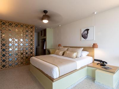 Modernes Schlafzimmer mit großem Bett, hellem Holzmöbel, Deckenventilator und dekorativem Raumteiler.