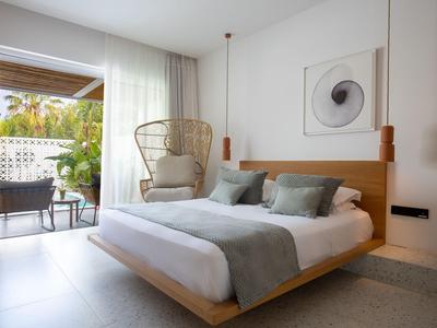 Modernes Hotelzimmer mit Doppelbett, Korbsessel und Zugang zu Terrasse mit Gartenblick.