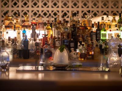 Bar mit vielen bunten Spirituosenflaschen und Gläsern vor einem hell beleuchteten Wandregal.