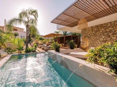 Moderner Außenbereich mit klarem Pool, Steinmauer, Pergola und tropischen Pflanzen bei Sonnenlicht.