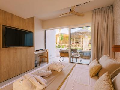 Helles Schlafzimmer mit Holzakzenten, großem Bett, Wand-TV und Zugang zu einer Terrasse mit Sitzbereich.